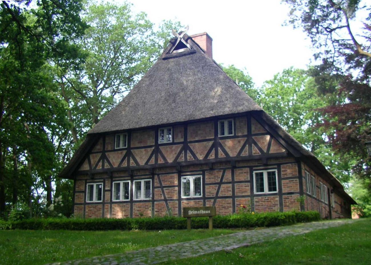 Heimathaus Jesteburg mit Strohdach und Fachwerk vor einem grünen Waldhintergrund.
